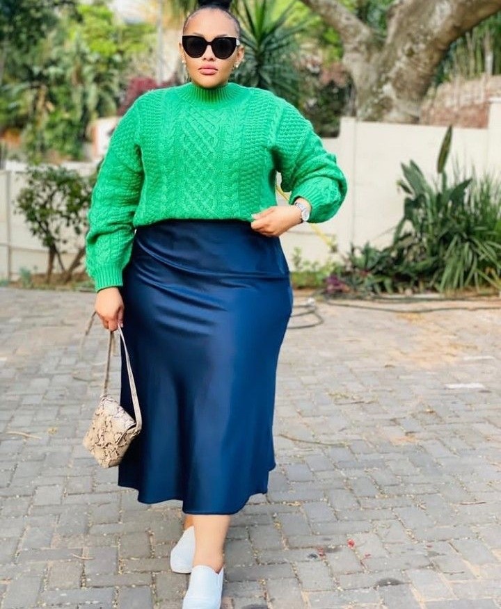 Woman wearing a chunky sweater with a satin midi skirt for an elegant fall outfit idea.