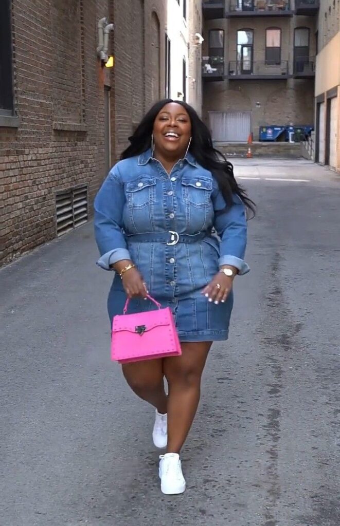 Plus-size woman wearing a denim shirt dress with white trainers.