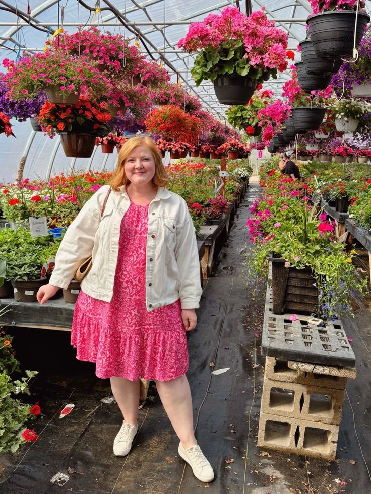 Plus size woman wearing a floral midi dress with a cropped denim jacket and white sneakers.