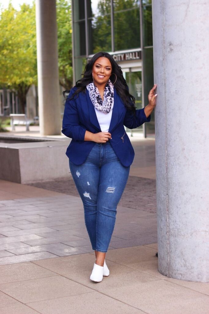Plus size woman wearing high-waisted jeans with a tailored blazer and white sneakers.