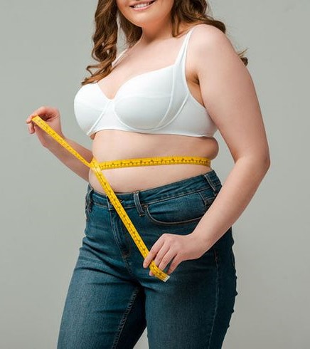 Plus-size woman using a measuring tape to measure her waist while identifying her body shape.