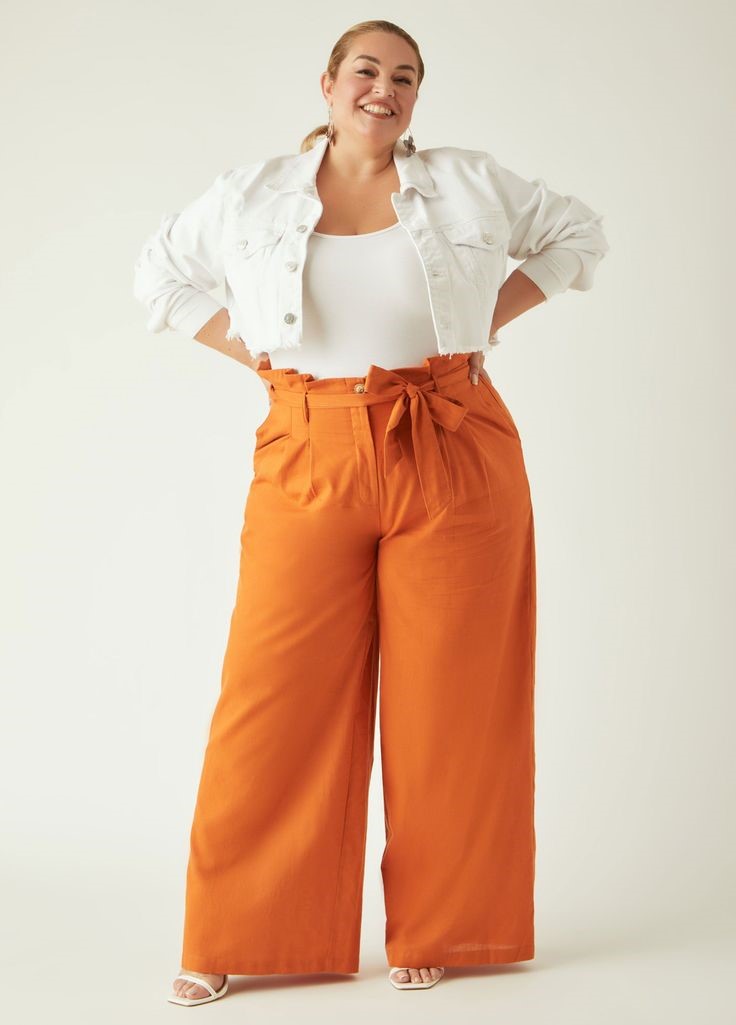 Plus-size woman wearing orange paperbag waist wide-leg trousers with a white tank top and cropped jacket for a stylish office outfit.