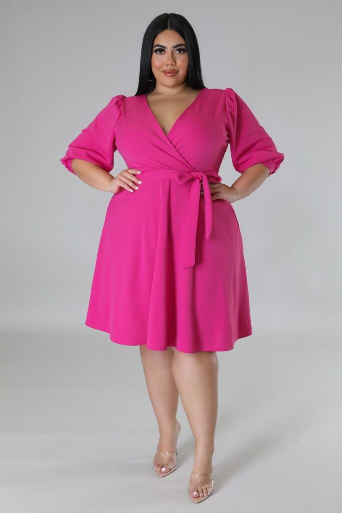 Plus size woman wearing a bright pink classic wrap dress with a V-neckline, waist tie, and three-quarter sleeves