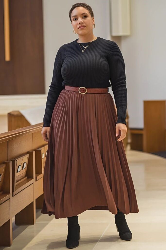 Plus size woman wearing a pleated midi skirt with a fitted turtleneck and ankle boots.