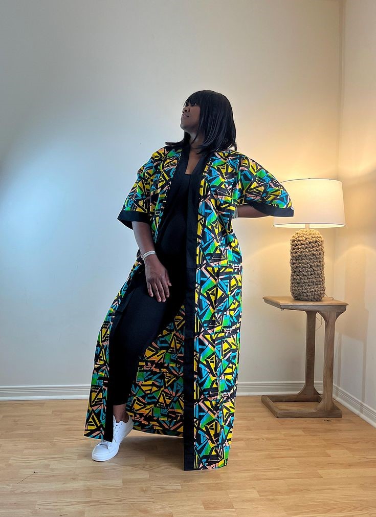 Plus-size woman wearing a colorful African print Ankara kimono over a black outfit with white sneakers.