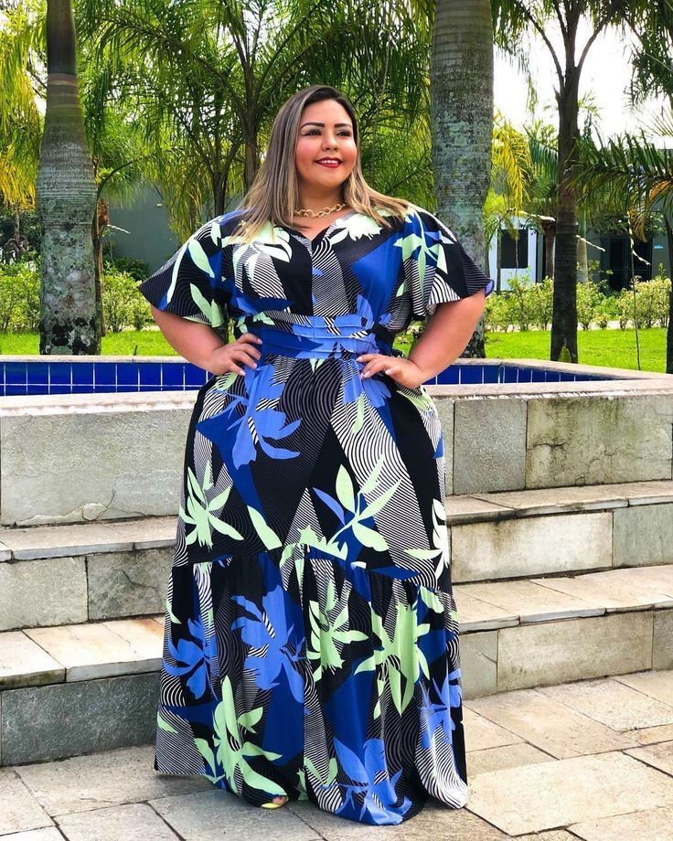 Plus-size woman wearing a blue tropical leaf print maxi dress with flutter sleeves and a waist tie.