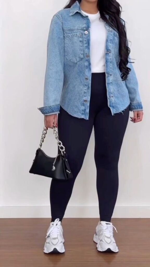 Plus-size woman wearing a denim shirt over a white top with black leggings and sneakers for a casual rainy-day outfit.