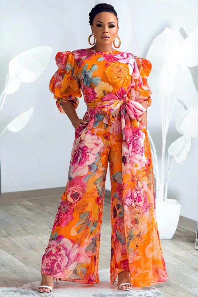 Plus-size woman wearing a bold orange floral statement jumpsuit with puff sleeves and a waist tie.