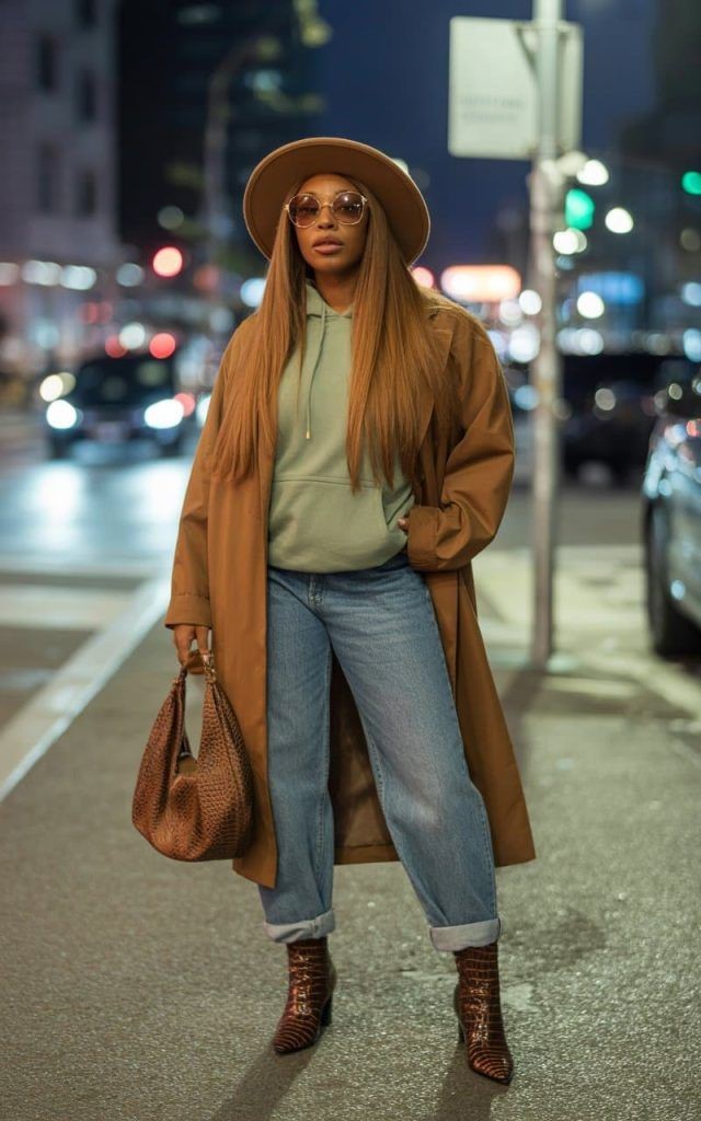 Plus-size woman wearing a long coat, hoodie, jeans, and ankle boots for a stylish rainy-day street style outfit.