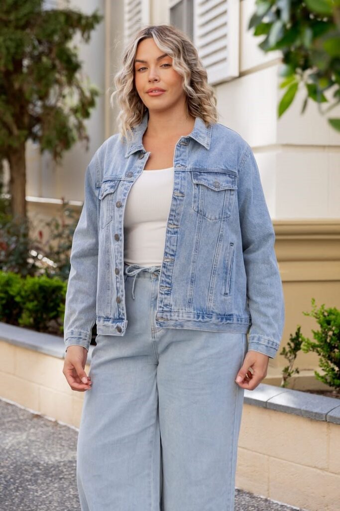 Plus-size woman styling a white T-shirt, light wash jeans, and denim jacket for spring.