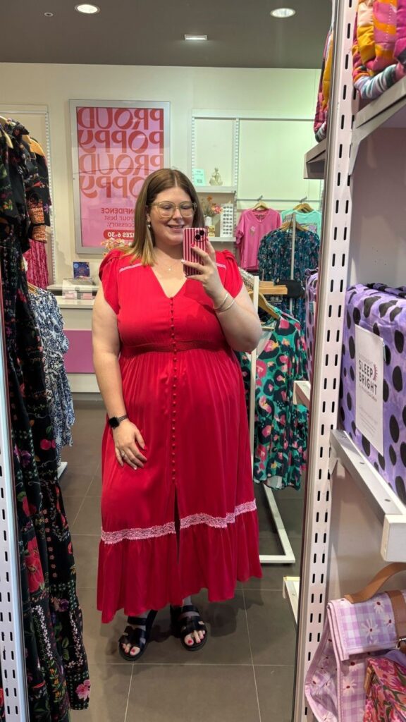 Plus-size woman shopping for affordable plus-size fashion while trying on a red maxi dress in a clothing store.