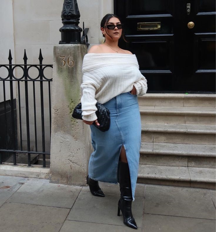 Woman wearing an oversized sweater with a denim midi skirt and knee-high boots for a stylish fall outfit idea.