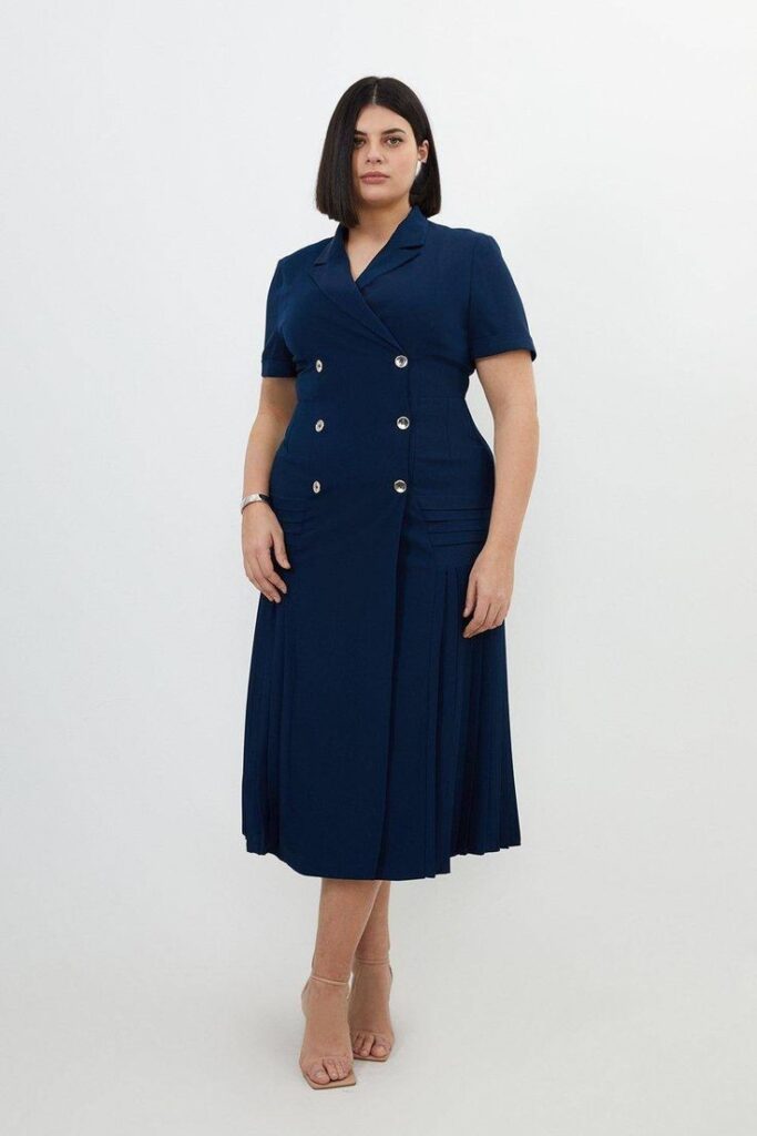 Plus size woman wearing a navy tailored shirt dress with a pleated midi skirt and nude heels for a business casual office outfit.