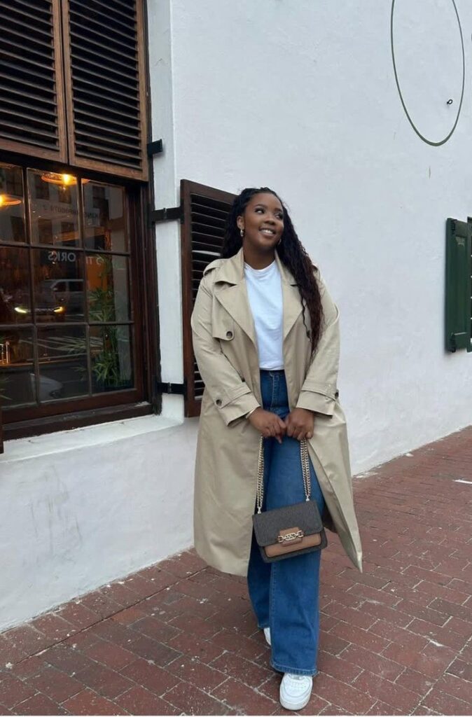 Plus-size woman wearing a beige trench coat with straight-leg jeans and white sneakers.