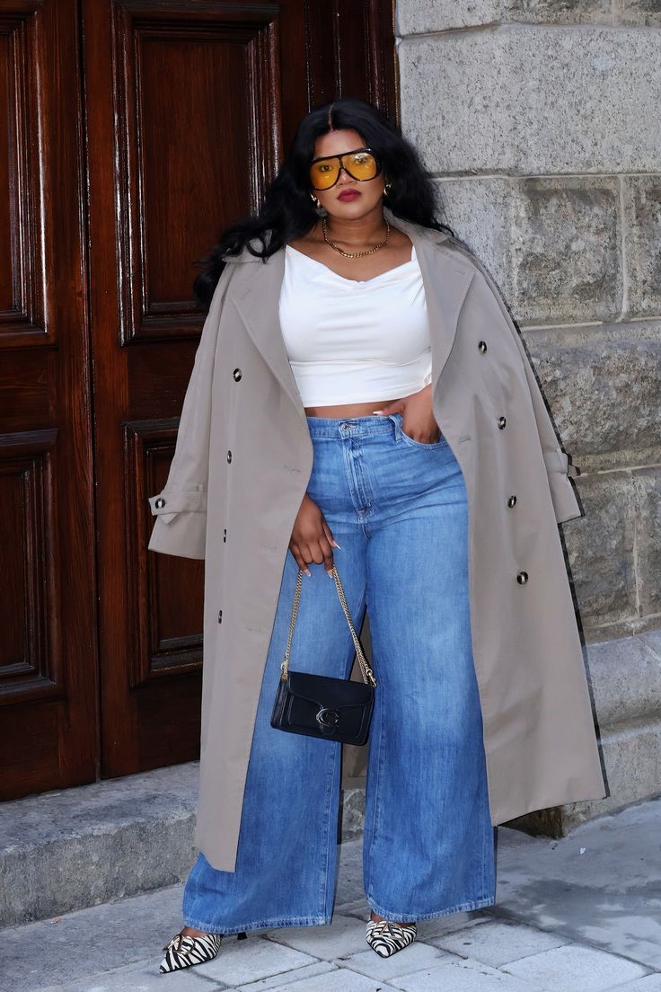 Plus size woman wearing wide-leg jeans with a beige trench coat and white sneakers.