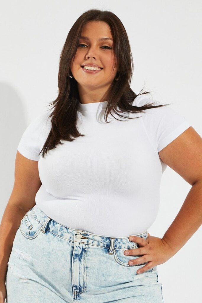 Plus size woman wearing a fitted white crew neck T-shirt with light-wash high-waisted jeans as part of a versatile wardrobe.
