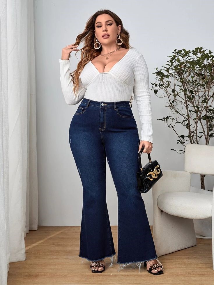 Woman wearing dark blue flared jeans with a white fitted top and black handbag