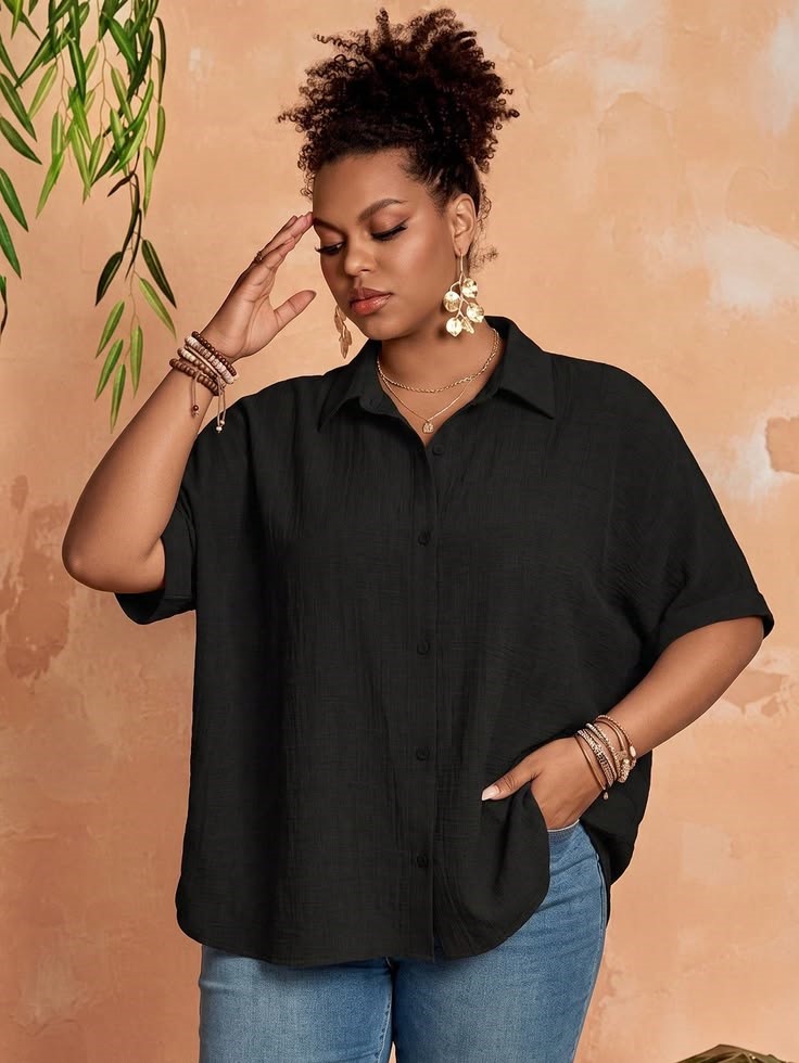 Plus size woman wearing a relaxed black button-front blouse with blue jeans, one of 30 versatile wardrobe pieces.
