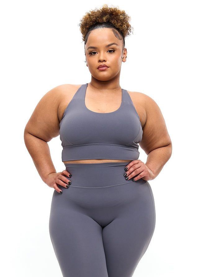 Plus-size woman with an inverted triangle body shape wearing a sports bra and leggings, showing shoulders broader than hips.