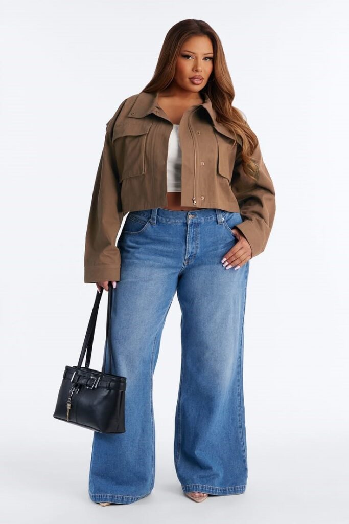 Plus size woman wearing a cropped khaki utility jacket over a white top with wide-leg blue jeans.