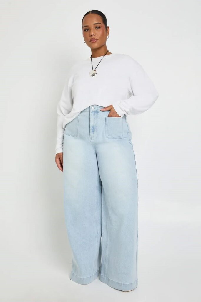 Plus size woman wearing light-wash wide-leg pants with a white long-sleeve top.
