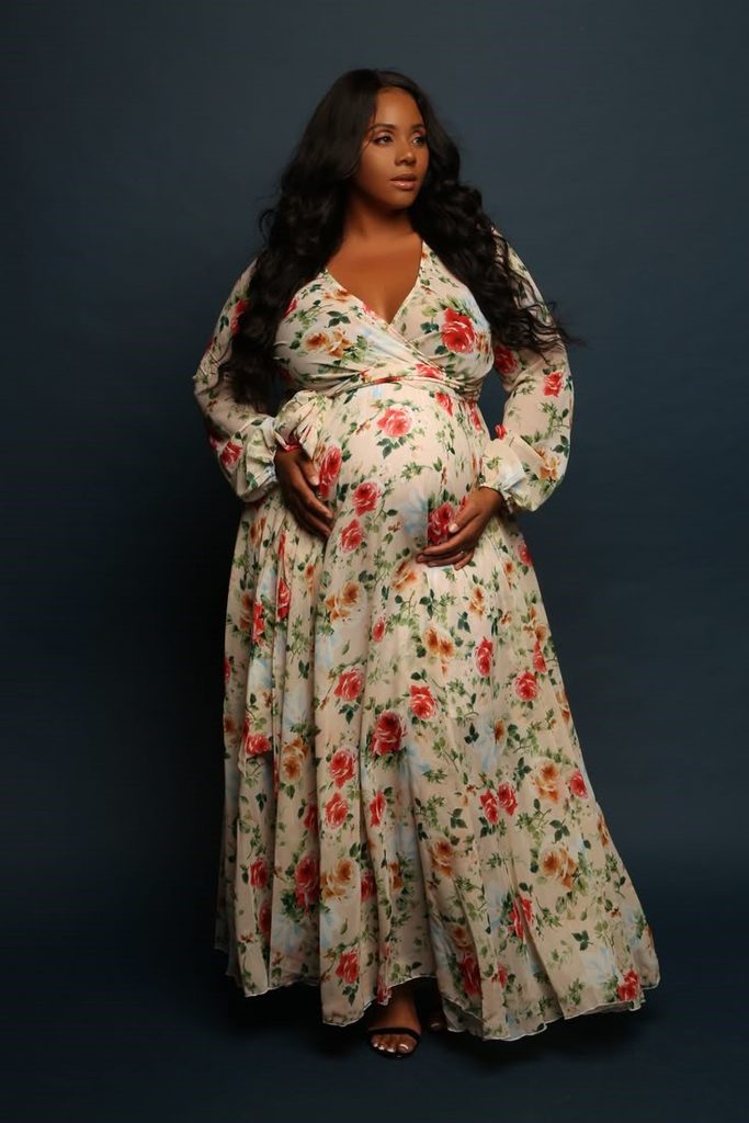 Pregnant plus size woman wearing a floral wrap maxi dress for a baby shower