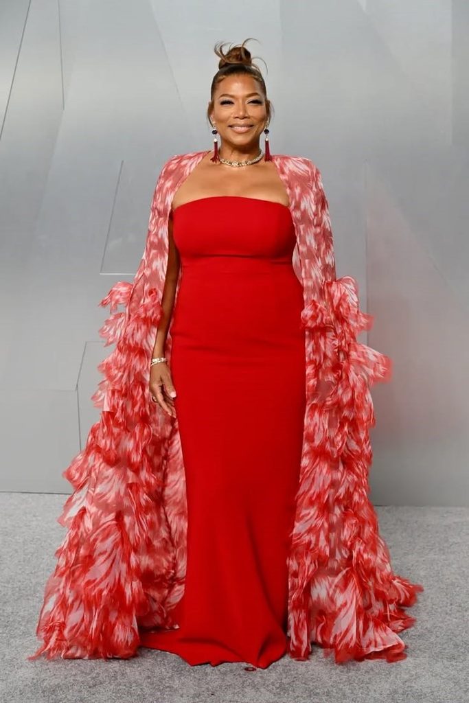 Queen Latifah wearing a red gown with a dramatic feathered cape at a red carpet event