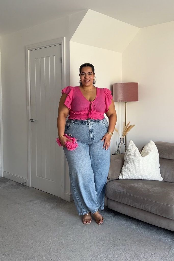 Plus-size woman in a pink top and wide-leg jeans showing why you can stop waiting to lose weight before dressing well
