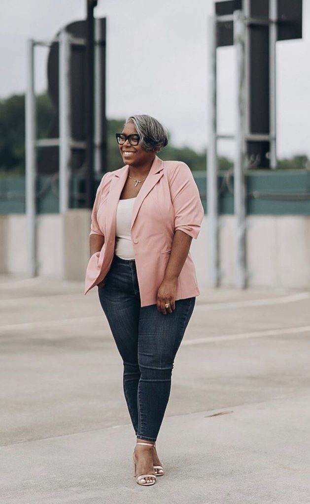 Plus-size woman in a pink blazer and jeans, showing why you can stop waiting to lose weight before dressing well