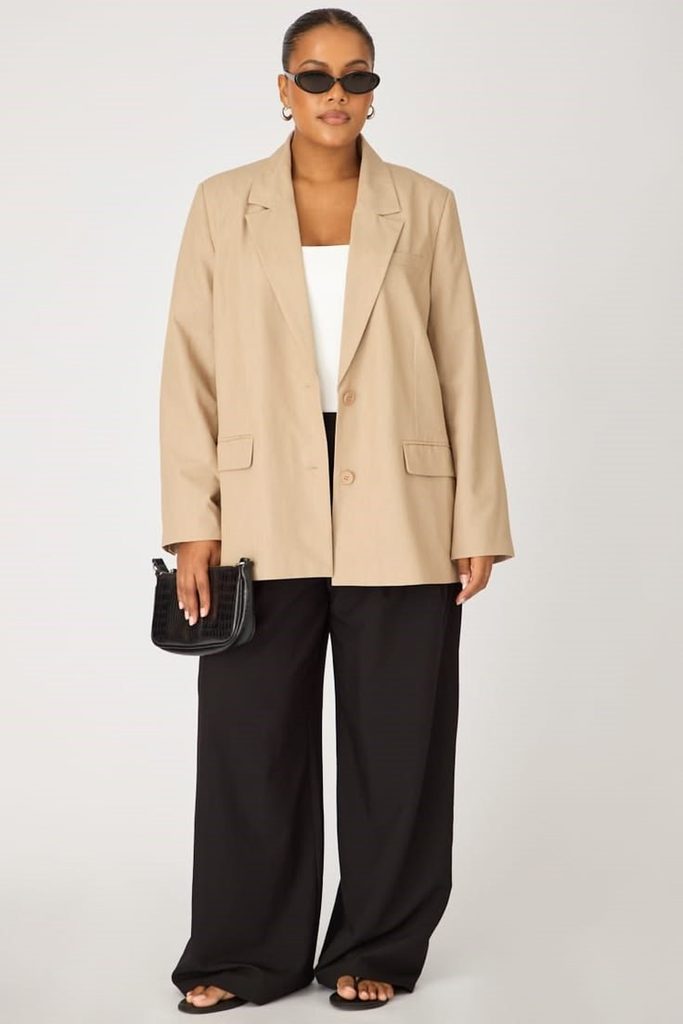 Plus size woman wearing a relaxed beige oversized blazer with black trousers