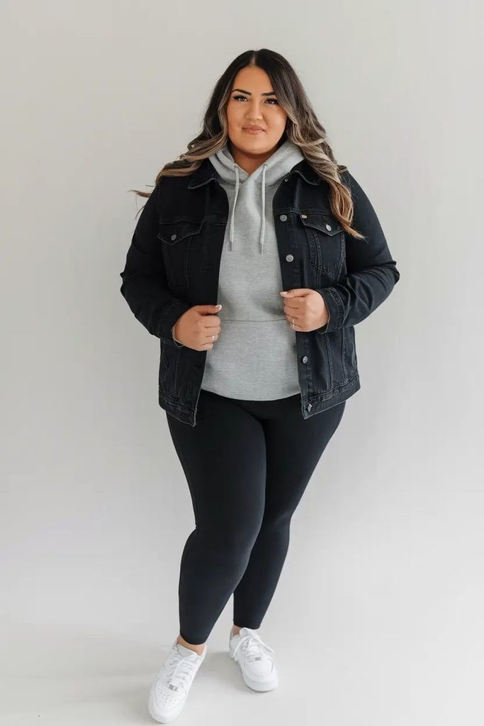 Cozy fall outfit for curvy women featuring a black denim jacket, grey hoodie, black leggings, and white sneakers