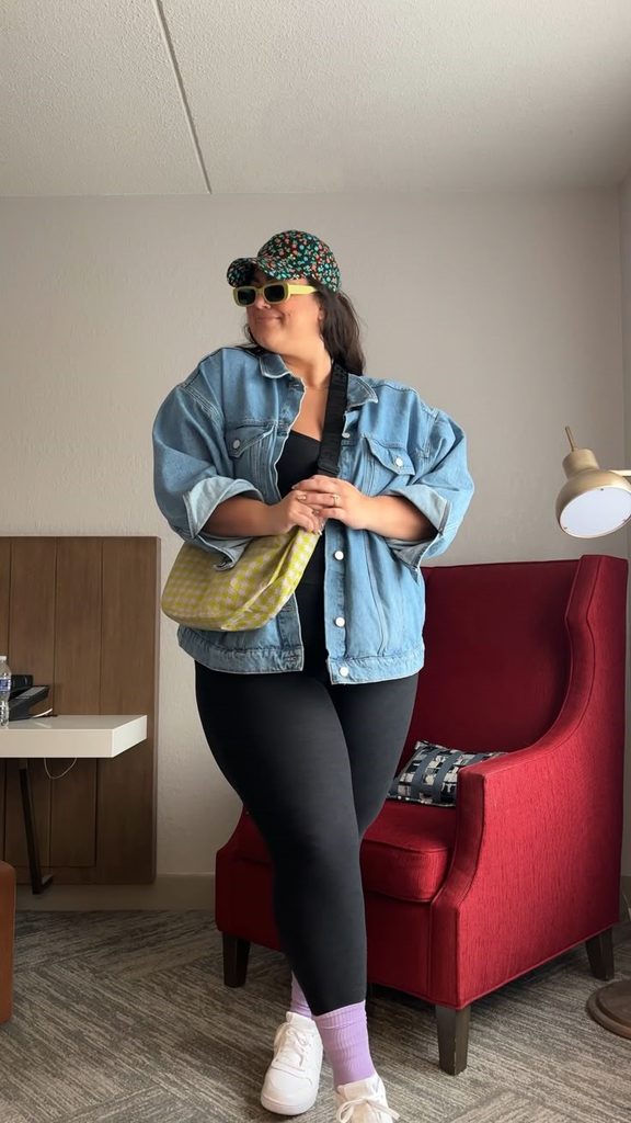 Plus size denim jacket outfit with black leggings, white sneakers, and a yellow shoulder bag.