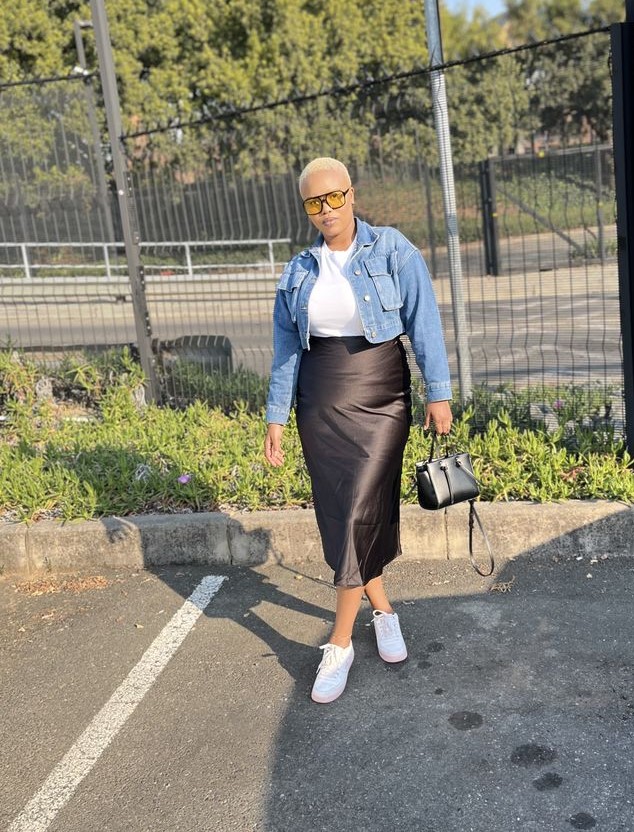 Denim jacket outfit with a black satin midi skirt, white fitted top, and white sneakers.