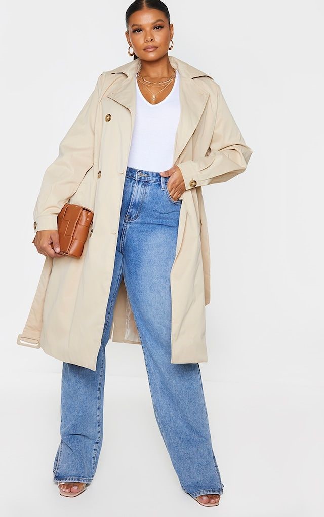 Plus size woman showing how to style a cream trench coat with blue wide-leg jeans and a white top.