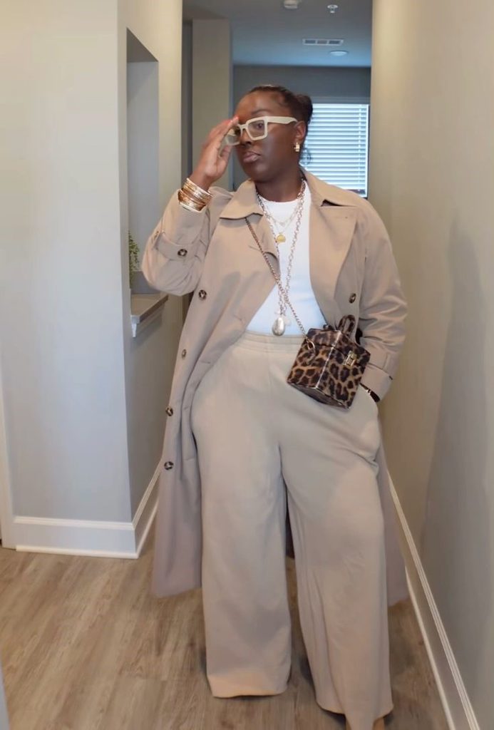 Plus size woman showing how to style a taupe trench coat with matching wide-leg trousers and a white top.