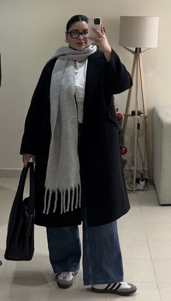 Long coat outfit ideas featuring a black long coat, oversized gray scarf, wide-leg jeans, and chunky sneakers