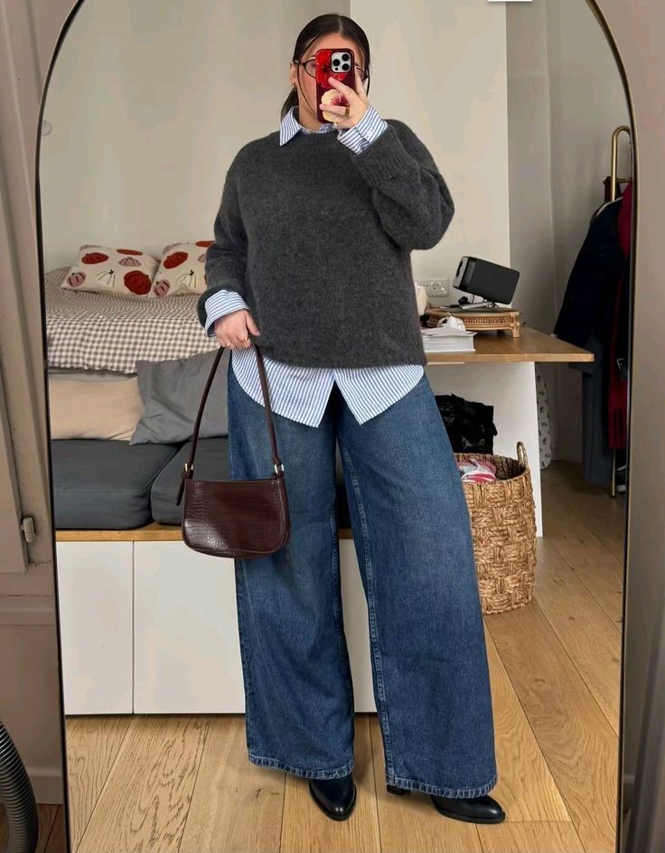 Plus size fall outfit featuring a charcoal grey sweater layered over a blue-and-white striped button-down shirt, wide-leg blue jeans, and black shoes.