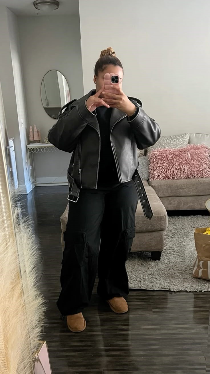 Plus size leather jacket outfit ideas featuring a black leather jacket, black cargo pants, black top, and brown slip-on shoes