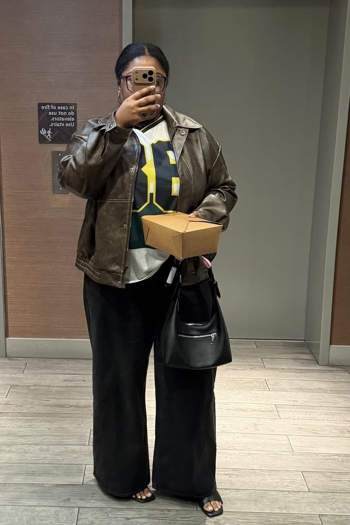 Plus size leather jacket outfit ideas featuring a brown leather jacket, sporty jersey, and black wide-leg trousers