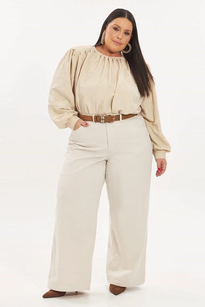 Minimalist fashion for plus size women featuring a beige blouse, cream wide-leg trousers, and a brown belt.