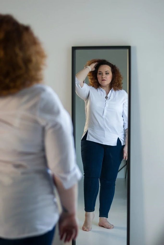 Plus size woman checking her outfit in the mirror while learning how to tell if you're wearing the wrong size