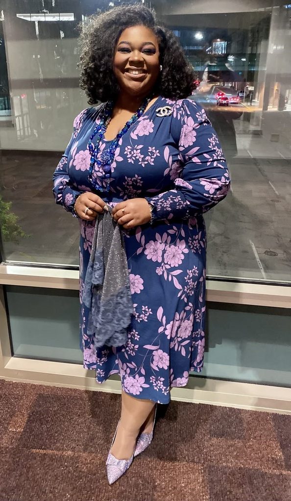 Plus size woman wearing a floral dress with multiple statement accessories.