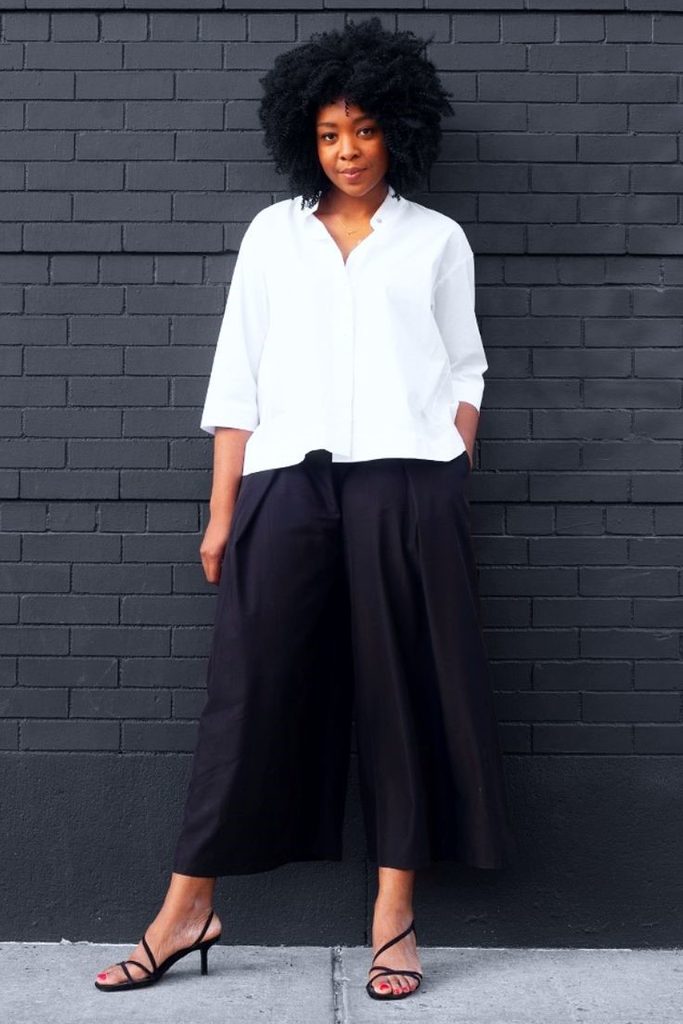 Plus size woman wearing a white button-down shirt with black wide-leg trousers and black strappy heels.
